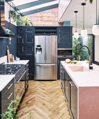 An open-plan kitchen with timber flooring, skylight, indoor houseplants and stainless steel refrigerator