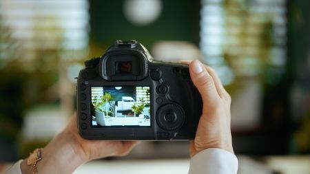 Closeup on woman real estate agent in green office in white blouse with dslr photo camera making interior photo.