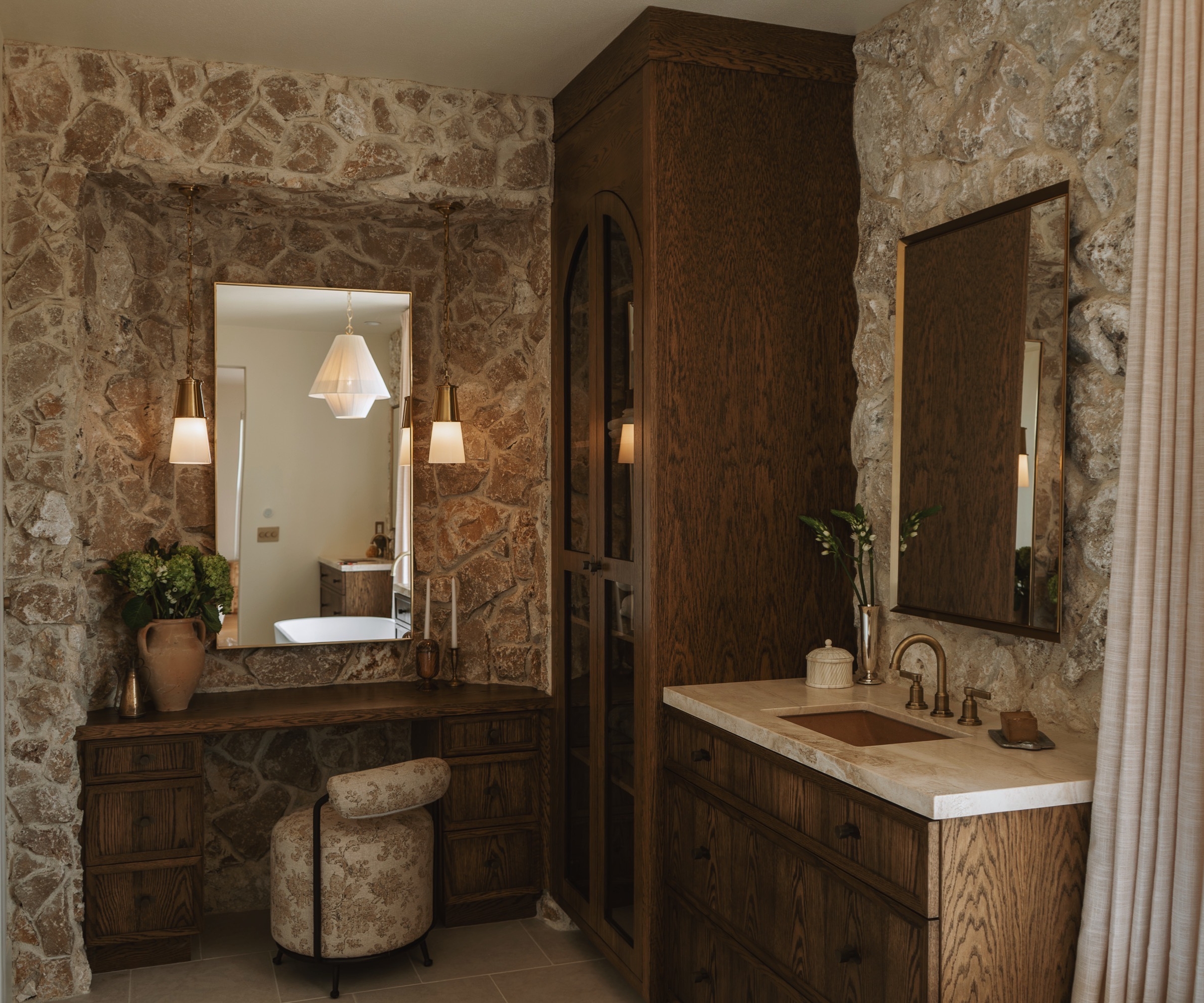 A warm neutral bathroom with exposed stone walls, dark wood cabinetry and vanity, and marble accents