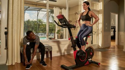 Echelon Smart Connect EX3 Max Exercise Bike review: a woman works out on the bike whilst a muscular man watches on