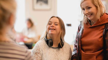 Over the shoulder view of a young female adult with down syndrome standing at a coffee shop counter ordering food and drinks.