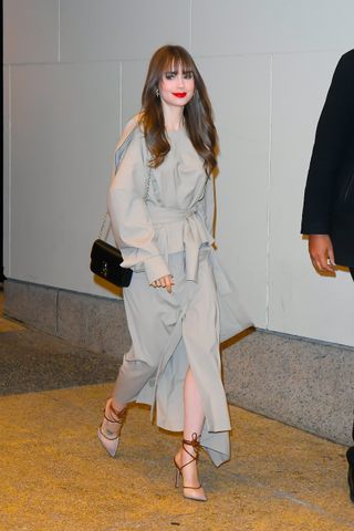 Actress Lily Collins is seen in SoHo on March 22, 2022 in New York City leaving a press event wearing a neutral asymmetric top and skirt from A.W.a.K.E. Mode with a Cartier Double C De Cartier Chain Bag, and neutral Andrea Wazen Denver wrap pumps