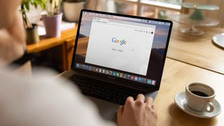 person in cafe about to search Google on MacBook