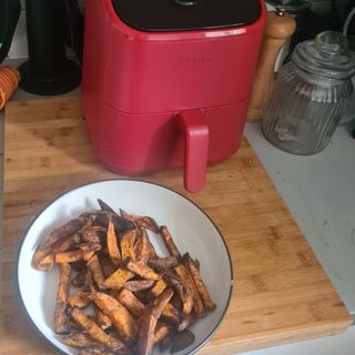 Pink Instant Vortex Mini Air Fryer next to bowl of sweet potato chips on wooden cutting board