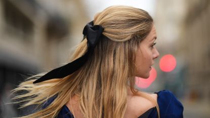 Mathilde Frachon wears gold earrings, a navy blue velvet silk short dress, and a bow in her blonde hair during a street style fashion photo session, on December 03, 2022 in Paris, France.