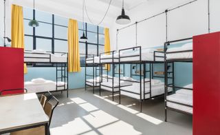 Hostel-style room with multiple bunk beds, a small desk with chair and yellow curtains at the window