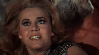 Jane Fonda as Barbarella smiling while being carried through the air
