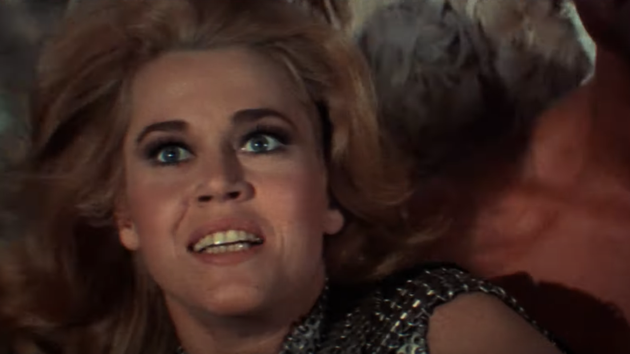 Jane Fonda as Barbarella smiles as she is carried through the air