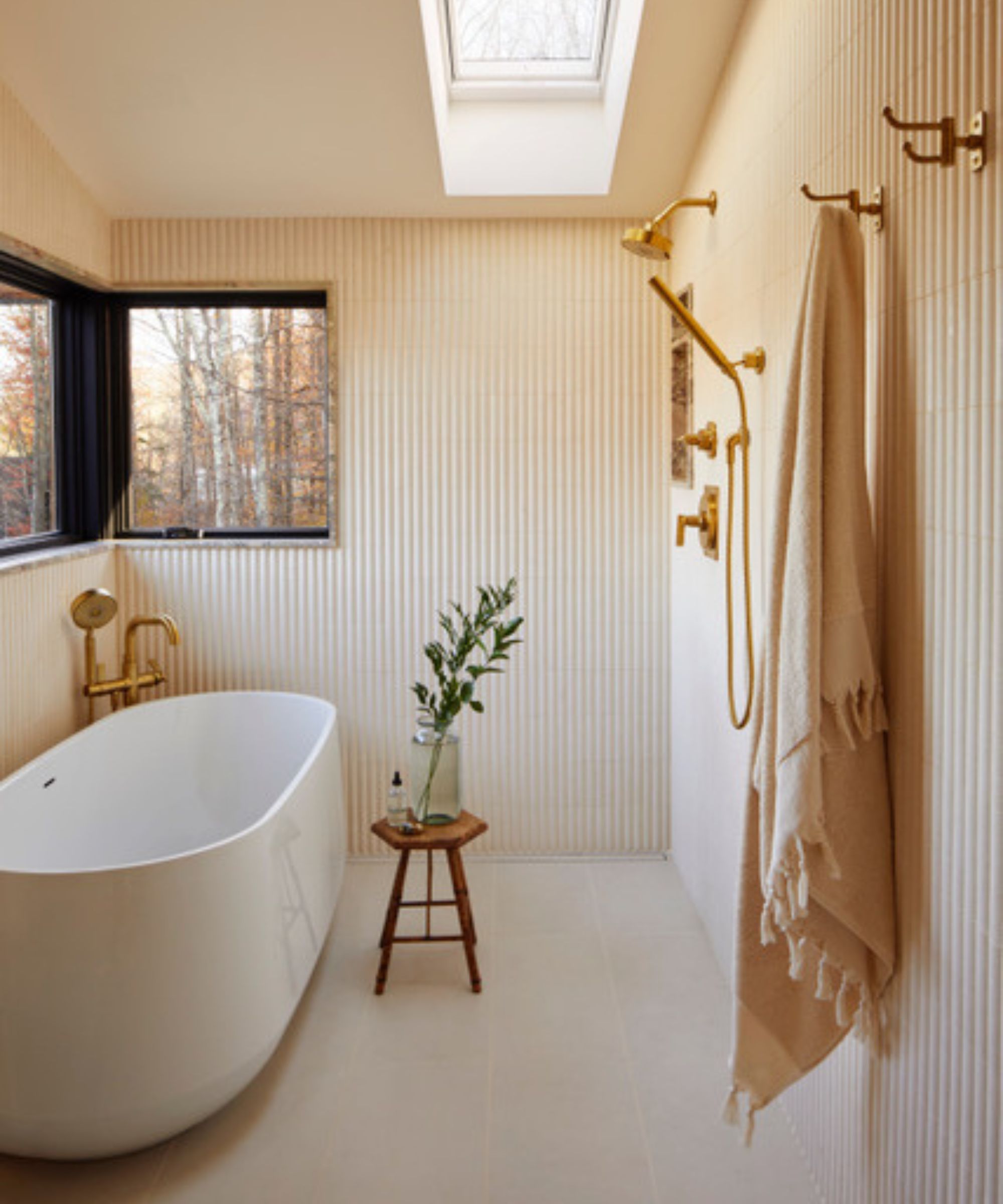 A wet room with striped walls, a freestanding tub, a gold shower and towel hooks, and a wooden bath stool