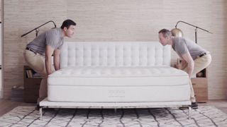 Two delivery men placing the Saatva classic mattress down on a bed frame