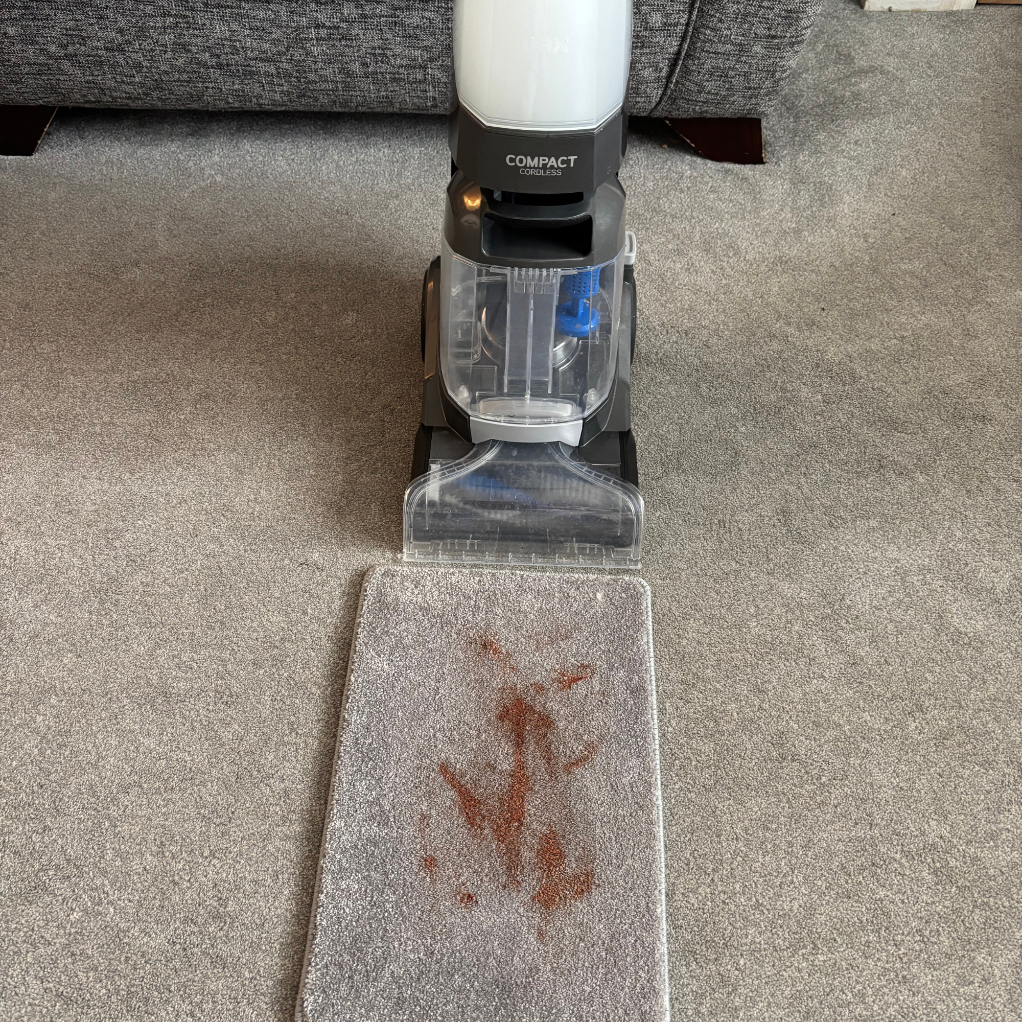 ONEPWR Cordless Compact Carpet Cleaner in front of carpet sample covered in ketchup