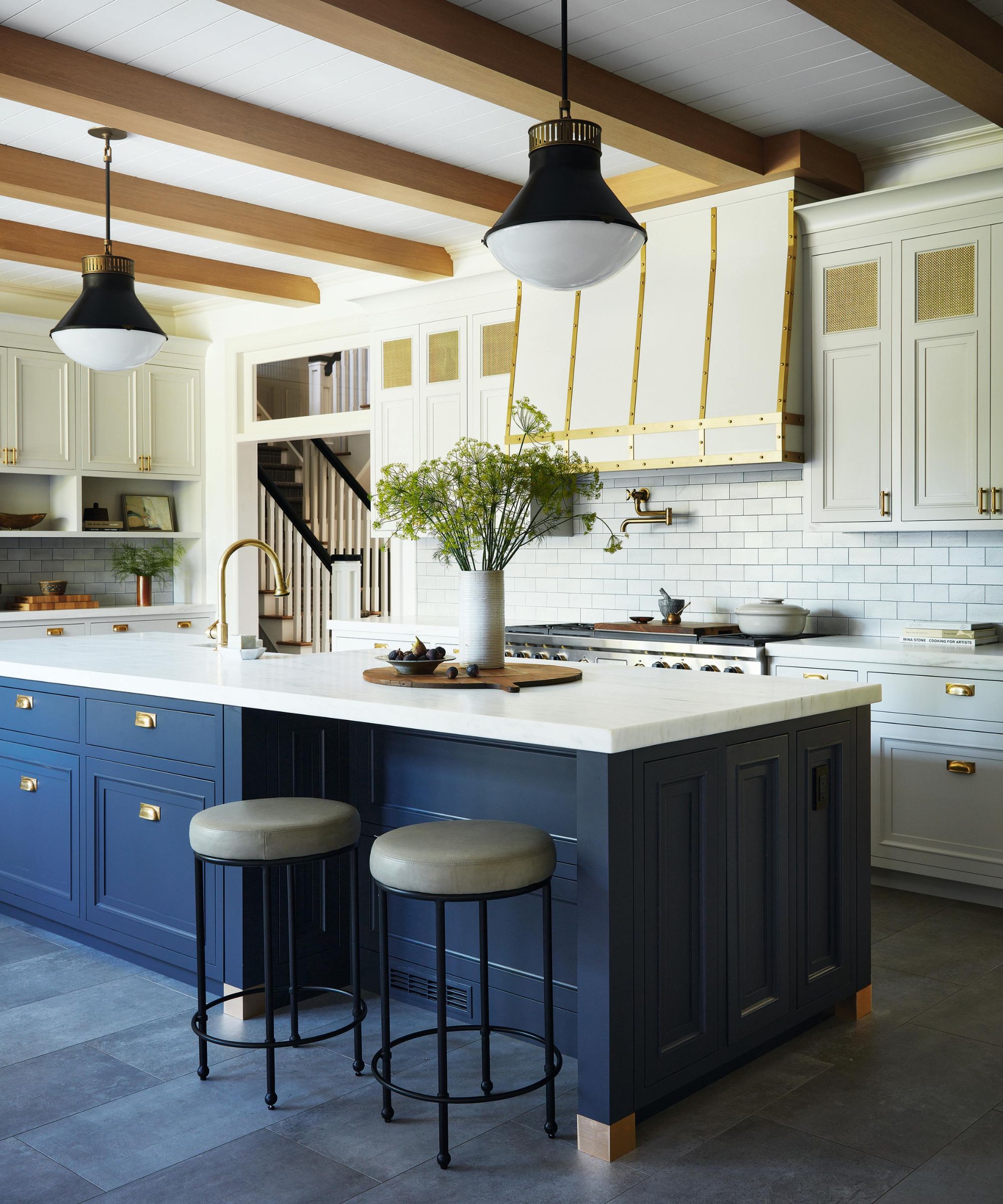 a white kitchen with a large navy island, ceiling beams and a large cooker hood with metal detailing