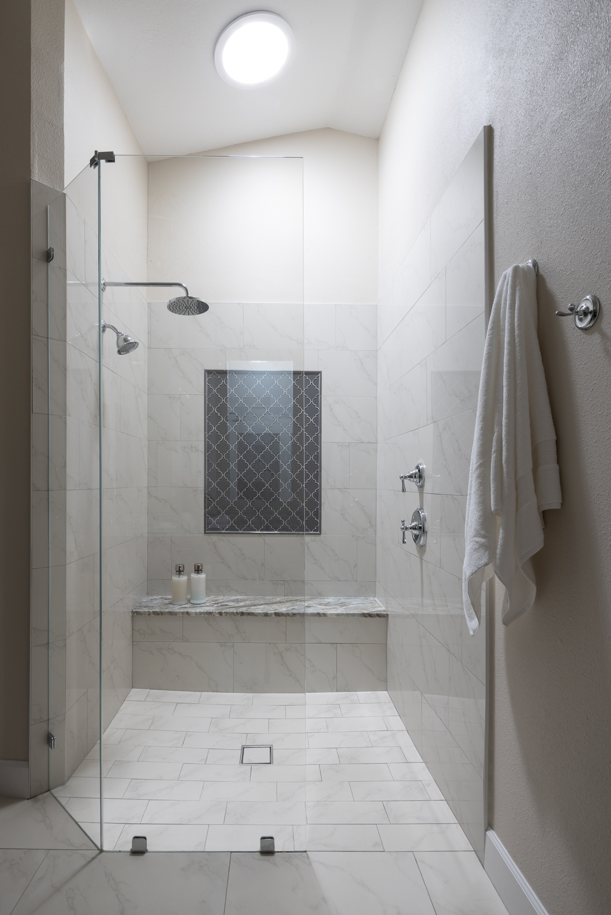 modern shower with bench seat, window, glass screen, towel hanging outside the shower, and round skylight