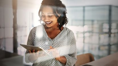 A smiling young woman in an office looks at her tablet.