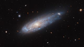 a blue and dark red misty galaxy in space, among many stars and other galaxies.