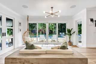 White sunroom with hanging chair and built-in sofa for two with green sofas, overlooking an outdoor pool