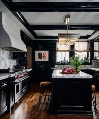 black and white kitchen with black cabinets and marble countertop and splashback, black island, brown barstools, stainless steel range and wooden floor