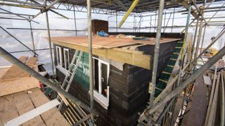 A black clad extension to a loft with scaffolding around it