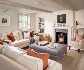 Cream fireplace and sofa, grey ottoman, orange cushions