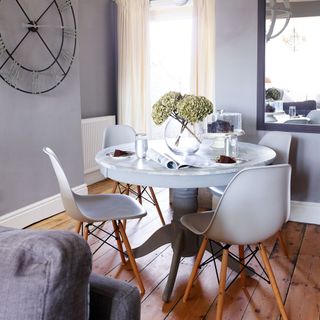 A small grey dining space with a round table, grey chairs and a large wall clock