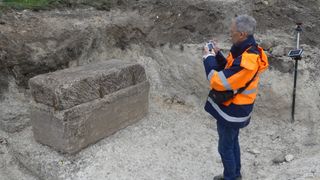 An archaeologist takes a picture of the free-standing stone sarcophagus.