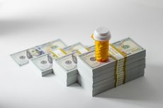 Prescription pill bottle with yellow tablets on growing stacks of US $100 bills, conceptual image representing pharmaceutical expenses, healthcare inflation and medication debt.
