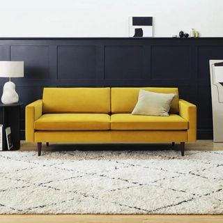 A mustard sofa in front of a blue wall