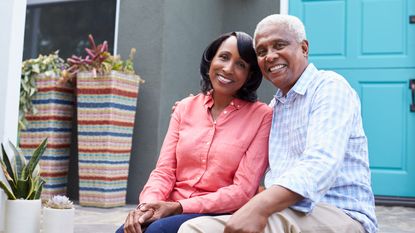 Smiling homeowners sit on the front porch of their house together.