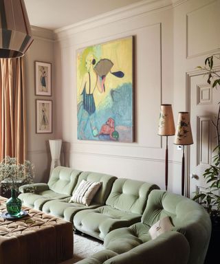 A light peach room with a green couch and a large piece of artwork hanging above