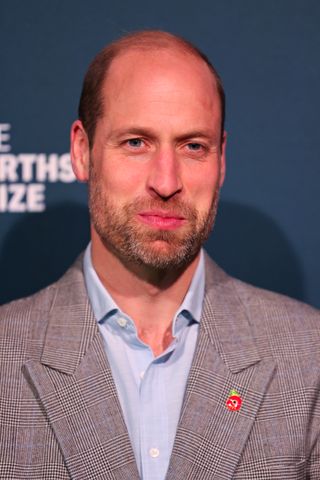 Prince William wearing a gray checked blazer and blue dress shirt smiling with his mouth closed