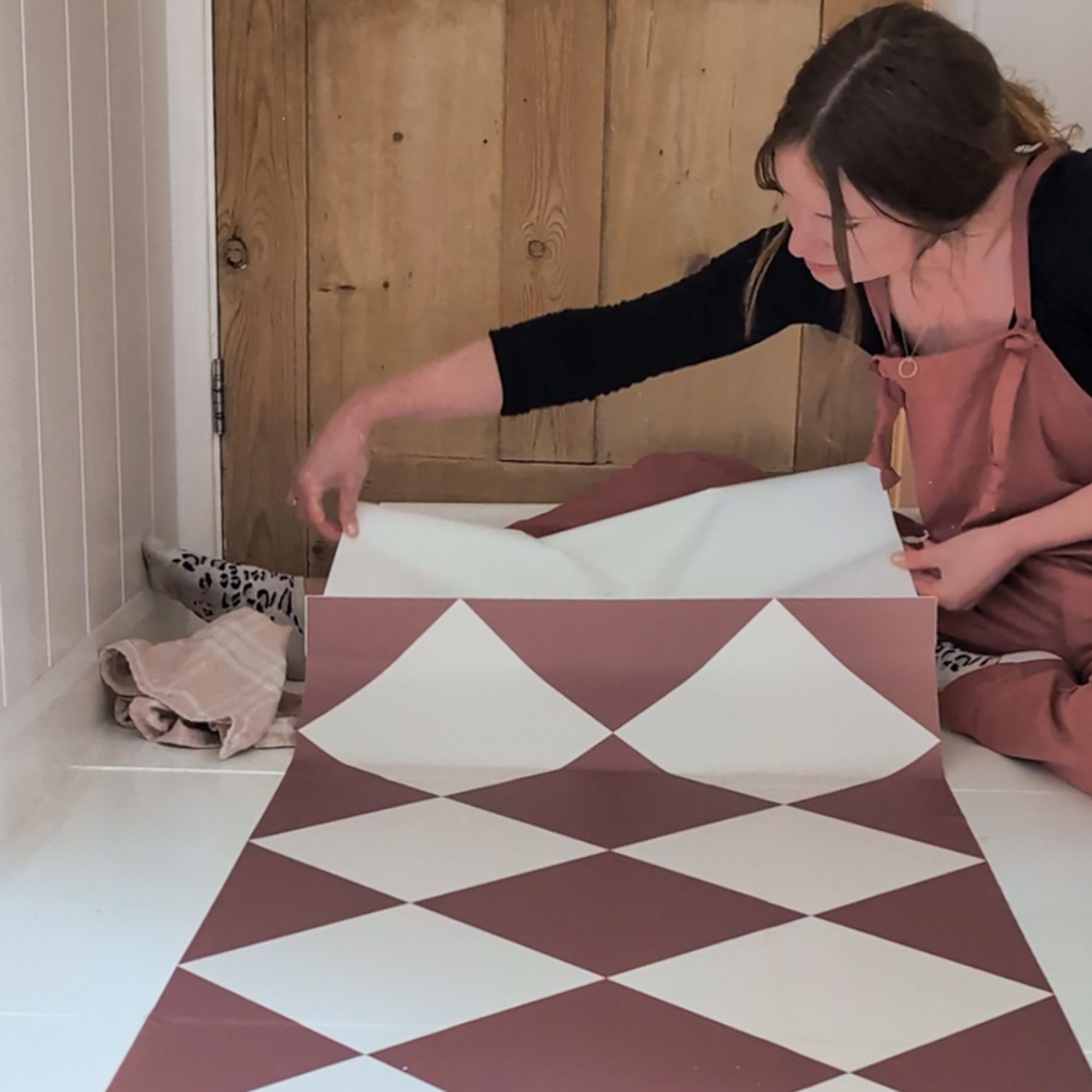 Lara Winter laying vinyl floor tiles with a terracotta and white checkerboard design in a small bathroom
