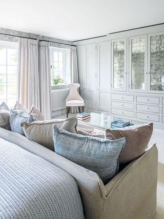 sofa with cushions in bedroom with fitted wardrobe in pale colors