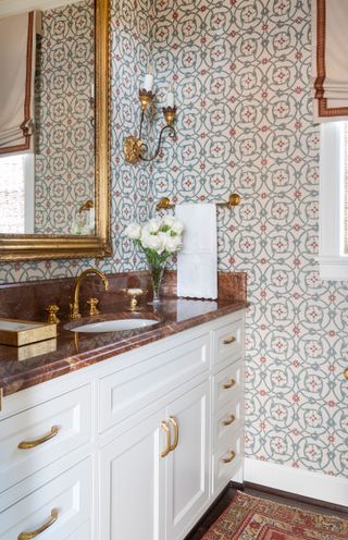 powder room with patterned tiles copper colored faucets and backsplash and white cabinets with mirror above and oriental rug on floor