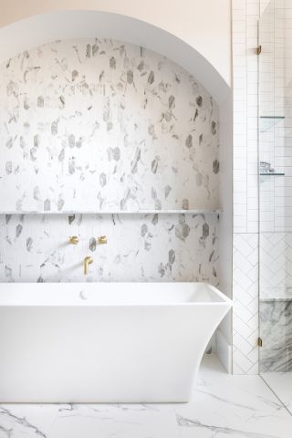 An example of spa bathroom ideas showing a white bathroom with different shaped tiles in marble and metro with a white bath