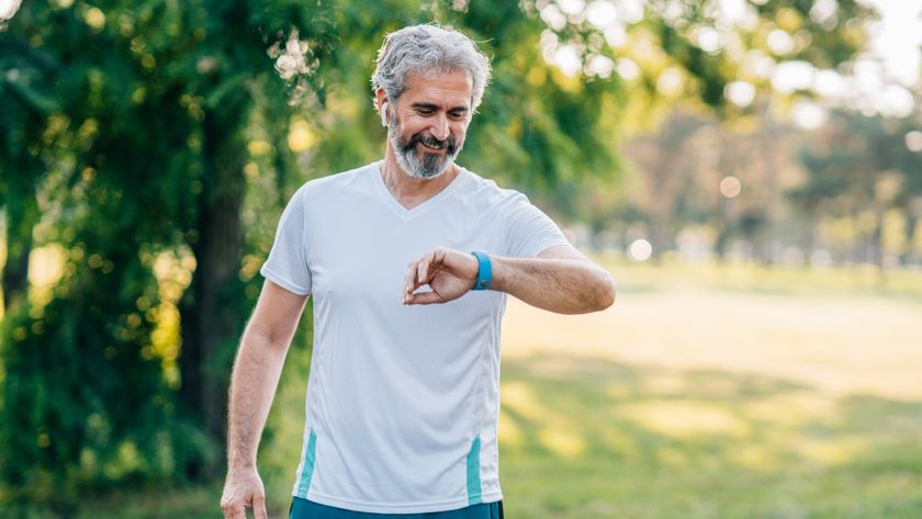 Older male outdoors smiling at his fitness tracker 
