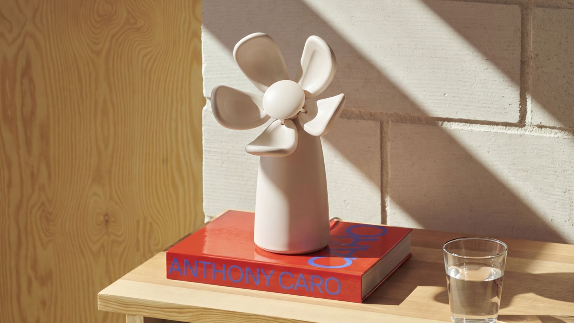 An off-white flower-shaped air quality checker from Bloomie on a wood shelf beside a glass of water and a colorful book