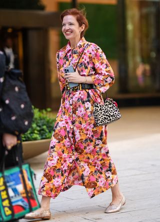 A guest wears dark pink floral pattern/print long sleeve midi dress, black leather belt with gold detail, light gray leopard pattern/print leather bag, a silver bracelet and gold shoes