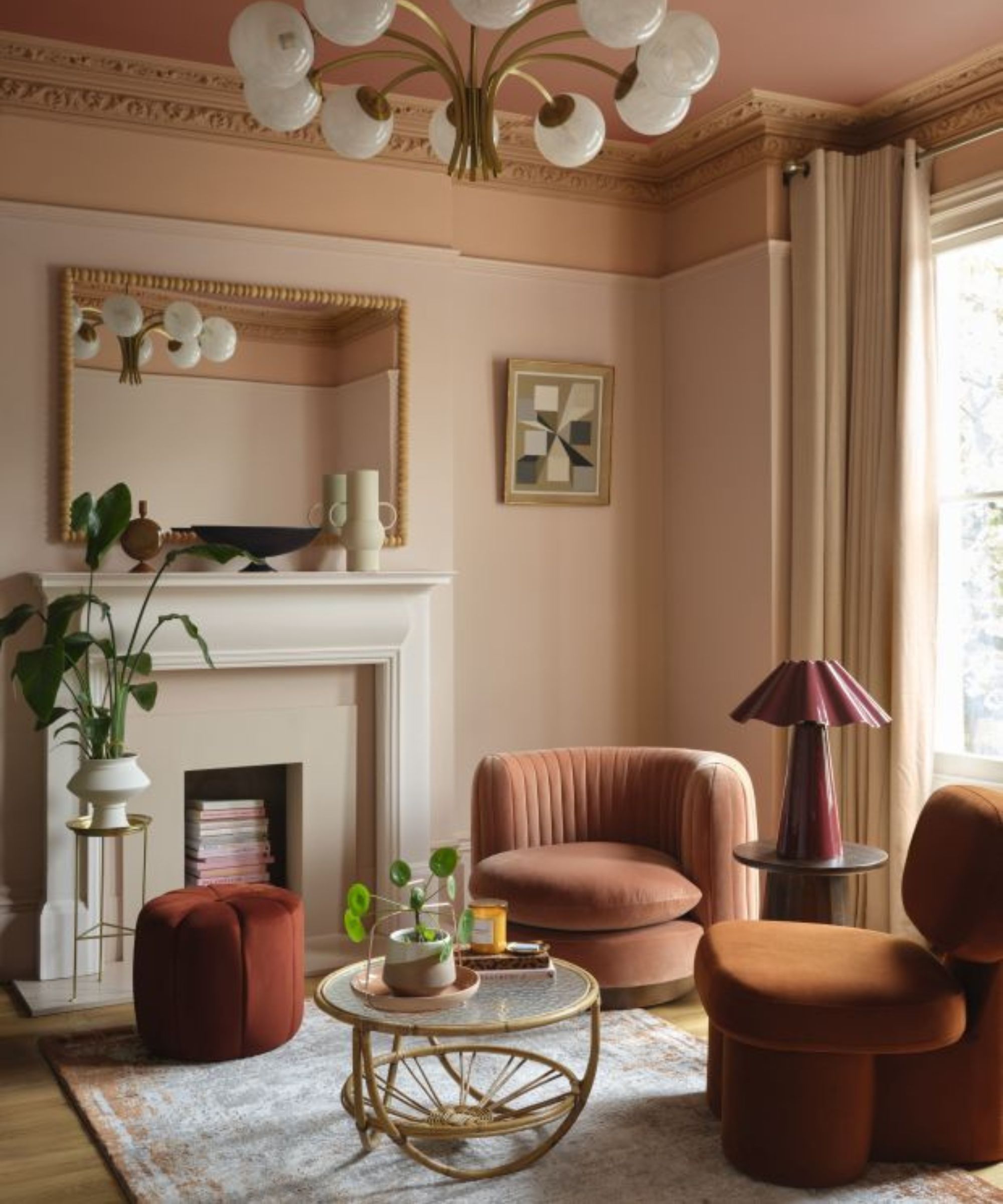 soft pink living room with a darker dusty pink painted ceiling and picture rail with a fireplace, bobbin mirror, pink velvet chair and burgundy lamp