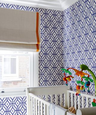 A nursery with blue and white geometric walls and white cot illustrating timeless boys' bedroom ideas