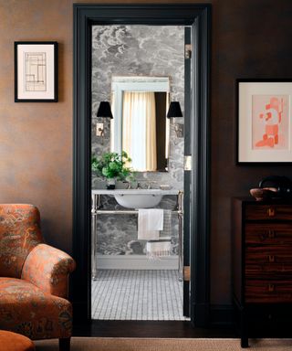 room with burnt orange walls and patterned chair though to monochrome bathroom