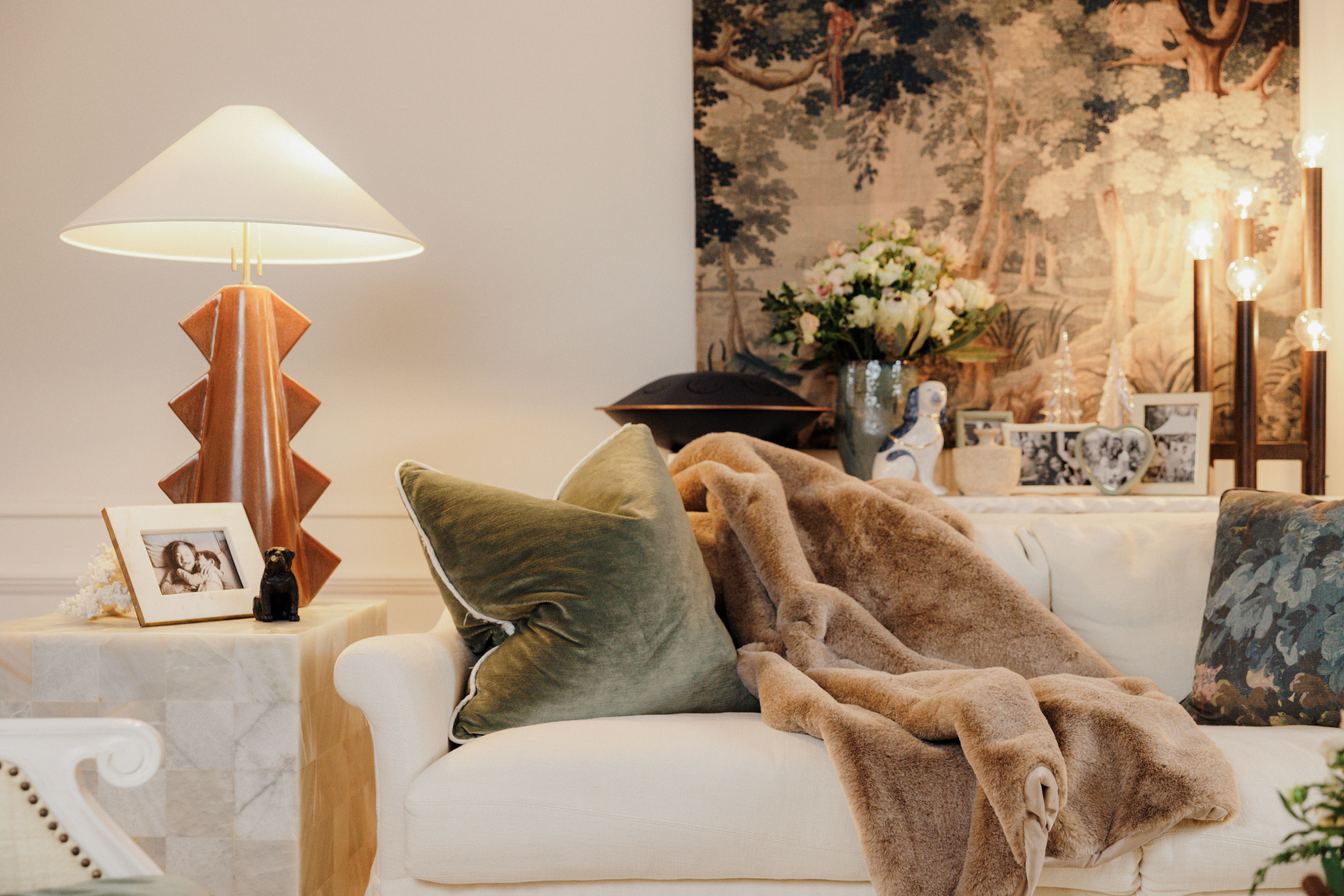 An earth-toned living room with a white coach, green pillows, and a brown fuzzy throw draped across the top.