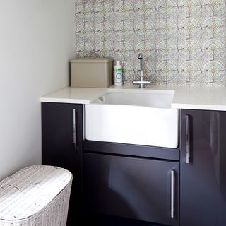 bathroom with wash basin with faucet and wallpaper on wall with brown cabinet