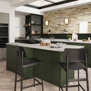 Kitchen with green cabinets and island and exposed brick wall, with the corner section of the kitchen separated by a black and transparent divider