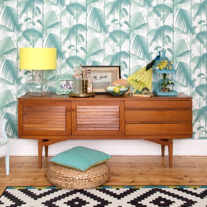 A living room with a tropical wallpaper and a mid-century modern sideboard
