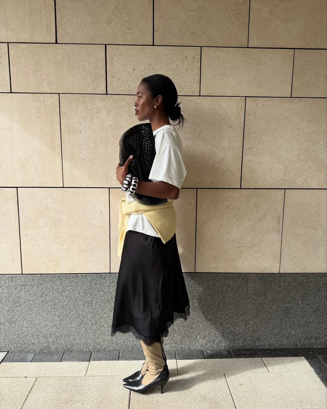 @nlmarilyn wears a black lace-trim slip skirt, white tee, yellow jumper, black leather clutch and mesh boots