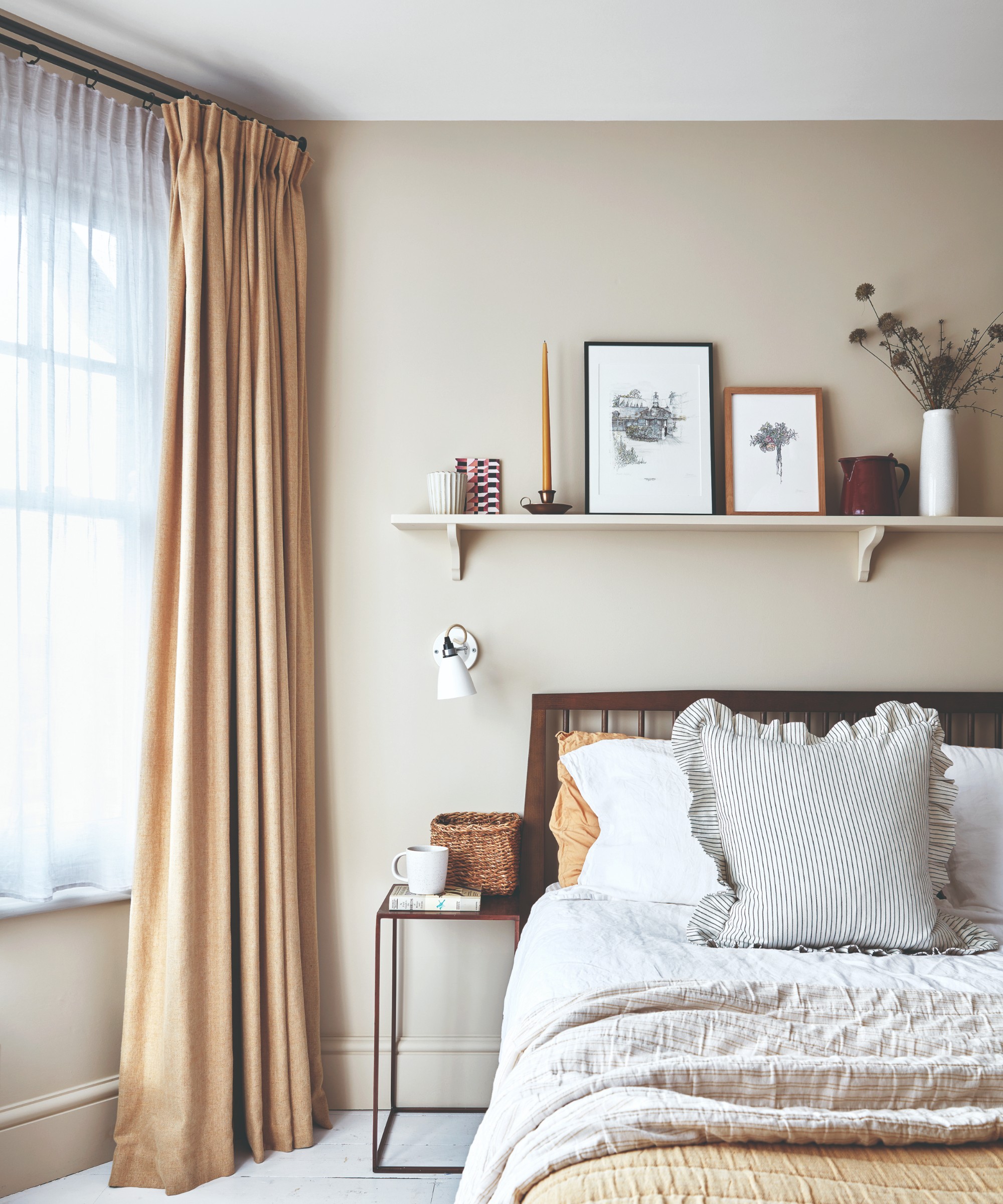 A neutral bedroom with a dark wooden bed frame and the window dressed in beige curtains and shorter white voile curtains