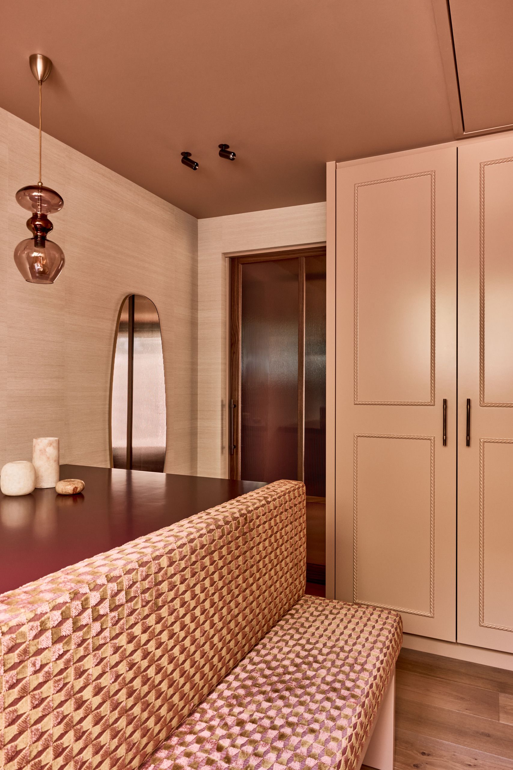 A dusty pink walk-in wardrobe with a pink patterned bench seat in the middle.