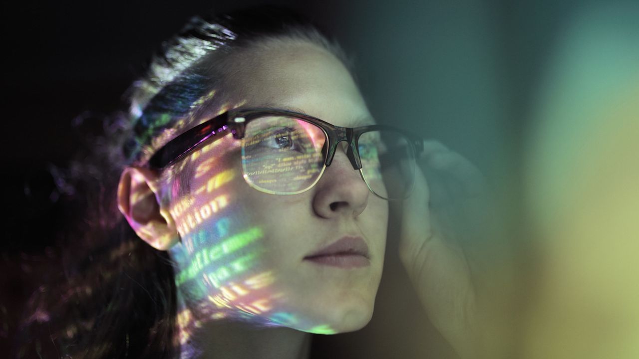 A thoughtful-looking young woman adjusts her glasses.