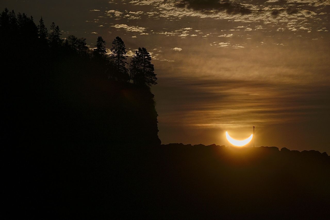 a partially eclipsed sun appears as a crescent shape and rising above the horizon at sunrise.