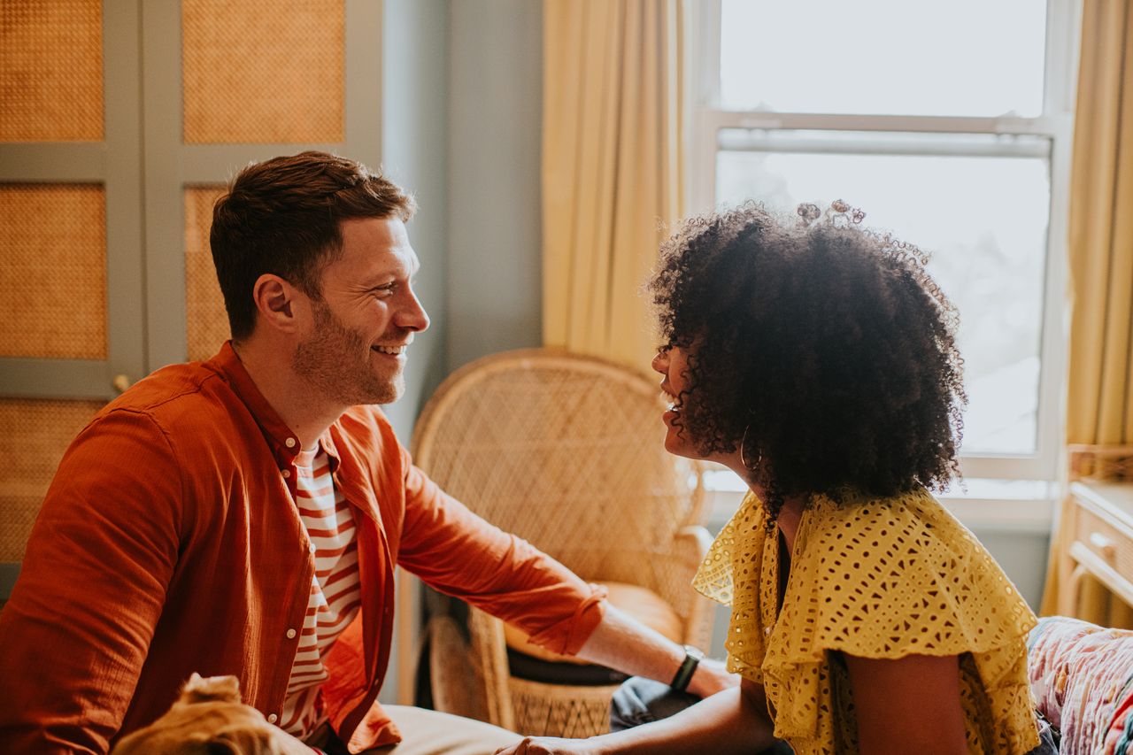 A couple in a stylish bedroom have an animated, and lighthearted discussion